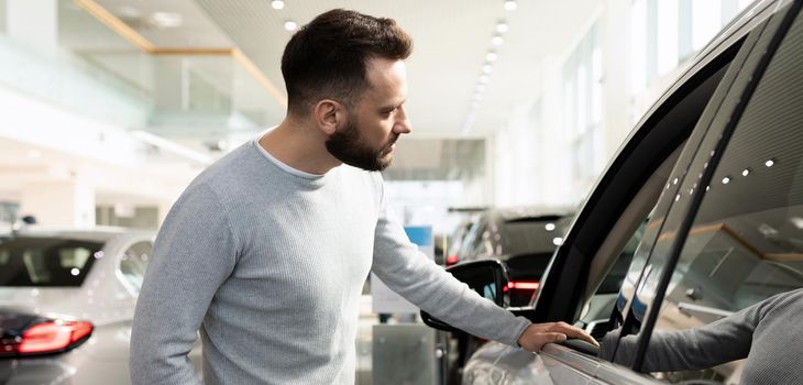 male buyer chooses a new car in a car dealership inspects the car.