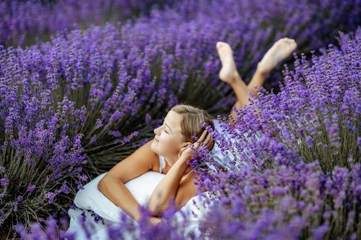 A middle-aged woman lies in a lavender field and enjoys aromatherapy. Aromatherapy concept, lavender oil, photo session in lavender.