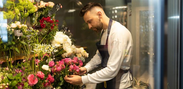 an experienced male florist in a bouquet shop examines the flowers in the fridge.