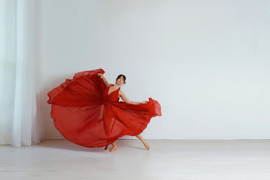 Dancer in a red flying dress. Woman ballerina dancing on a white studio background.