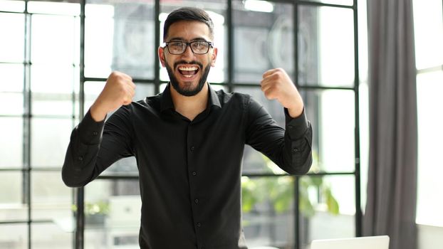 young businessman celebrating success in his home office holding fists up celebrating achievement