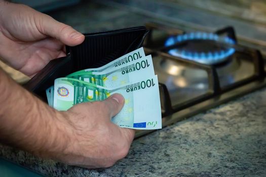 Close up of mens hands with a purse and euro banknotes on the background of a gas stove. A concept showing the energy crisis in Europe. Copy space