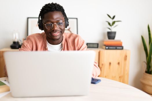 Front view of young African American man wearing headphones working, studying at home using laptop. Copy space. E-learning and technology concept.