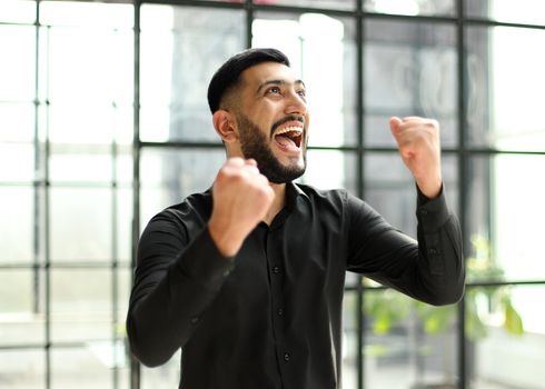 young businessman celebrating success in his home office holding fists up celebrating achievement