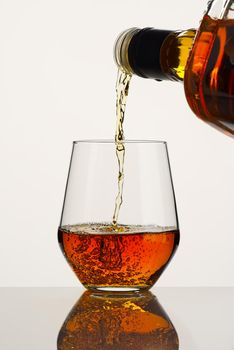 Pouring whisky from a bottle. whiskey being poured into a glass from bottle on white background. strong alcohol brandy, Cognac