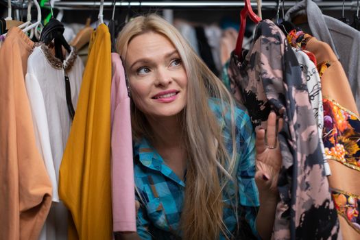 A European woman with Caucasian beauty creeps to hunt for the best clothes for this summer season. A smiling blonde among hangers of clothes.