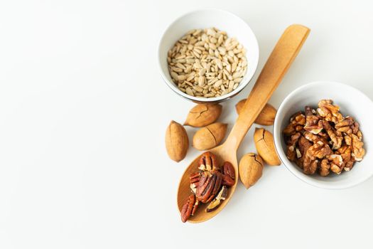 A close-up of a plate with different nuts and seeds along with a wooden spoon lie on a white table. The concept of weight loss, healthy eating, overweight. Fitness menu