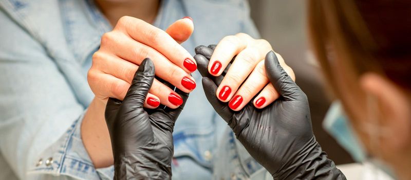 A manicurist holds beautiful young female hands showing finished red polish manicure in a nail salon