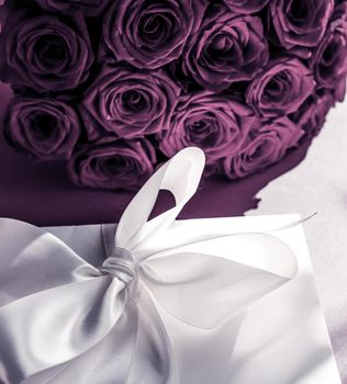 Happy holidays, luxe shopping and love gifts concept - Luxury holiday silk gift box and bouquet of roses on purple background, romantic surprise and flowers as birthday or Valentines Day present