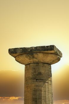 Ancient classical architecture Doric Greek column with grooved shaft and round flare on top, against a bright sun.