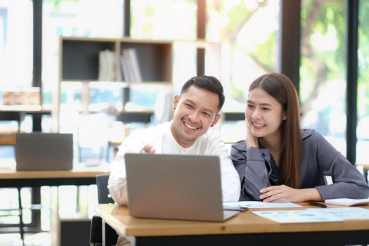 Two employees in a modern office, an Asian man and a woman working at a table, colleagues discussing and consulting, thinking about a joint project.