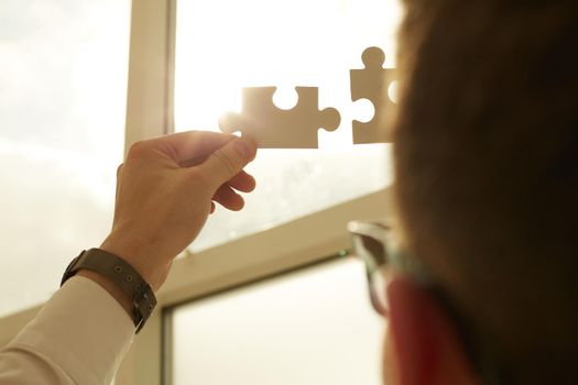 two hands of businessman to connect couple puzzle piece with sky background.Jigsaw alone wooden puzzle against sun rays