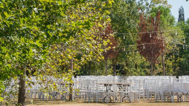 White chairs and tables in the autumn nature among the trees, outdoor event. High quality photo