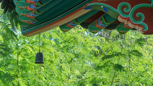 A bell on the roof of a Buddhist scar against a backdrop of green trees. High quality photo
