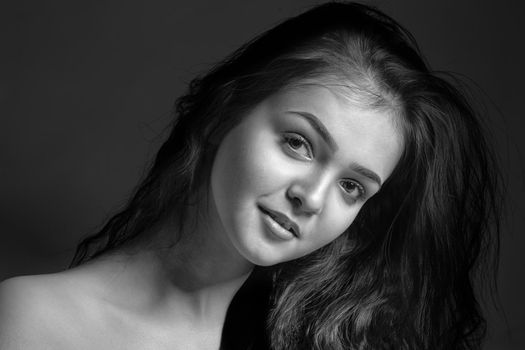 Monochrome portrait of a young attractive woman in the studio on a dark background.