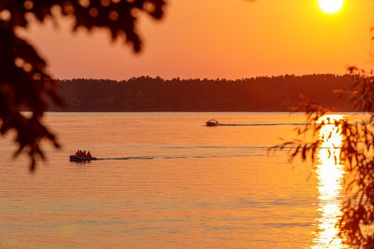 A boat pulls a person over the waves on a wakeboard. Wakeboarding at sunset.