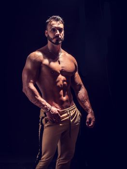 Shirtless muscular male bodybuilder in studio shot on black, with dramatic lighting
