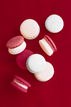 Pastry, bakery and branding concept - French macaroons on wine red background, parisian chic cafe dessert, sweet food and cake macaron for luxury confectionery brand, holiday backdrop design