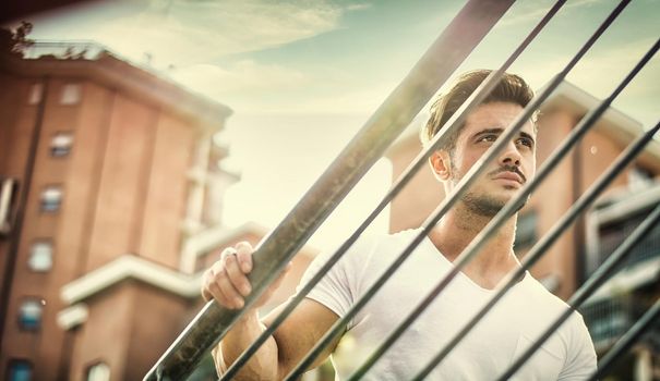 Handsome fit man in white t-shirt outdoor in city setting, climbing metal stairs, looking away