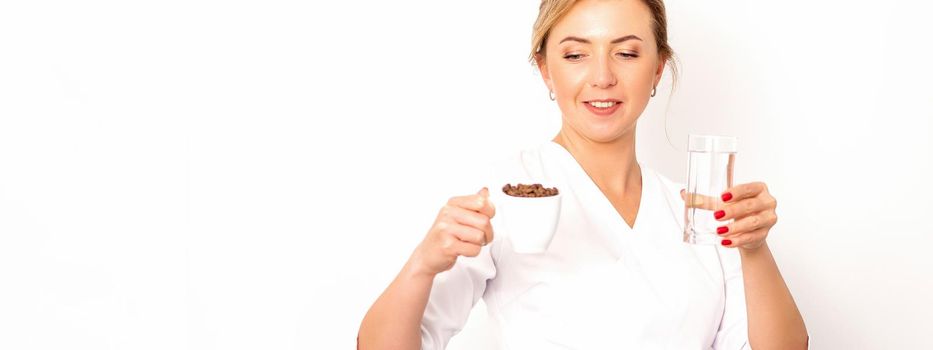 Coffee with water. The female nutritionist holds a cup of coffee beans and a glass of water in her hands on white background