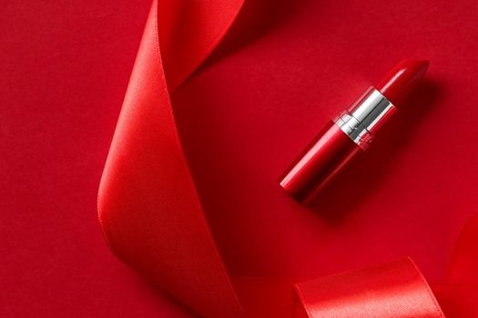 Cosmetic branding, glamour lip gloss and shopping sale concept - Luxury lipstick and silk ribbon on red holiday background, make-up and cosmetics flatlay for beauty brand product design