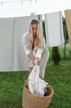 Laundry day. A woman hangs linen and towels on a tree in the courtyard of a village house. Summer cottage concept.