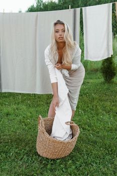 Laundry day. A woman hangs linen and towels on a tree in the courtyard of a village house. Summer cottage concept.