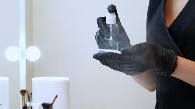 beauty saloon. close-up, the master in black special gloves holds a cotton pad and sprinkles it with an antiseptic. High quality photo