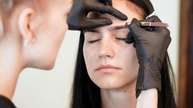 beauty saloon. close-up, hands of the cosmetician in black rubber gloves hold tweezers and pull out eyebrows. Master corrects the shape of the eyebrows. High quality photo
