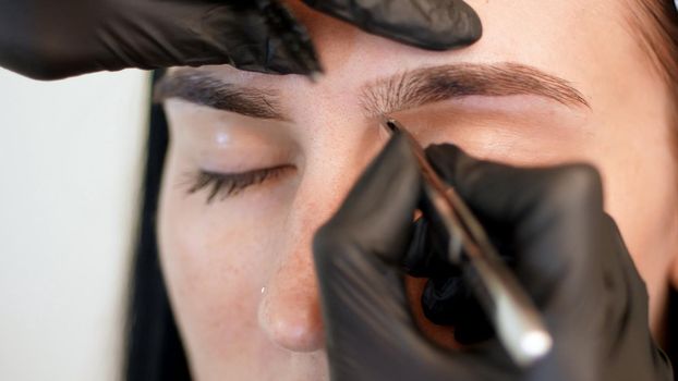 beauty saloon. close-up, hands of the cosmetician in black rubber gloves hold tweezers and pull out eyebrows. Master corrects the shape of the eyebrows. High quality photo
