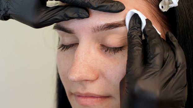 beauty saloon. a close-up, the master wipes the eyebrow area with a cotton disc moistened with antiseptic. High quality photo