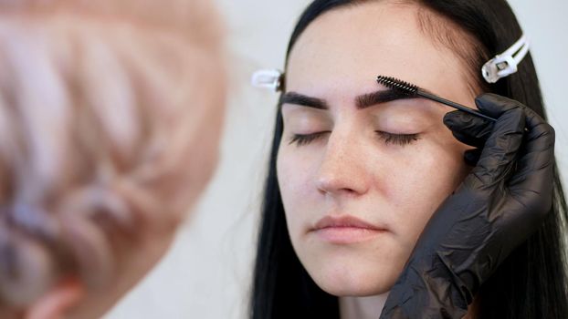 beauty saloon. close-up, a beautician in black rubber gloves, gently combs the eyebrows of the client with a special little brush, comb, shapes the eyebrows after staining. High quality photo