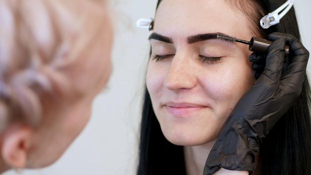beauty saloon. close-up, a beautician in black rubber gloves, gently combs the eyebrows of the client with a special little brush, comb, shapes the eyebrows after staining. High quality photo