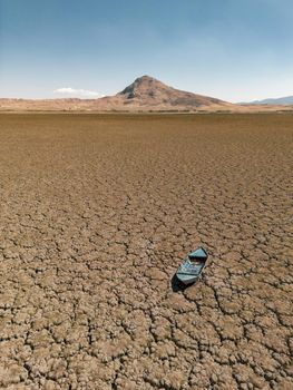 Abandoned row boat on cracked soil on lake bed dried up due to global warming and drought