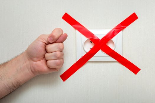 The man shows a fig gesture near the electrical outlet, tied with a red ribbon criss-cross. The concept of the energy crisis in Europe
