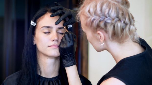beauty saloon. Eyebrow correction. cosmetologist, browmaker, master in black rubber gloves, draws with special pencil the shape of eyebrows before applying eyebrow dye. High quality photo