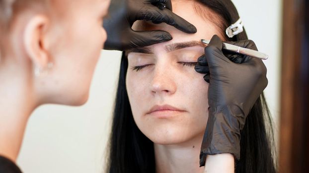 beauty saloon. close-up, hands of the cosmetician in black rubber gloves hold tweezers and pull out eyebrows. Master corrects the shape of the eyebrows. High quality photo