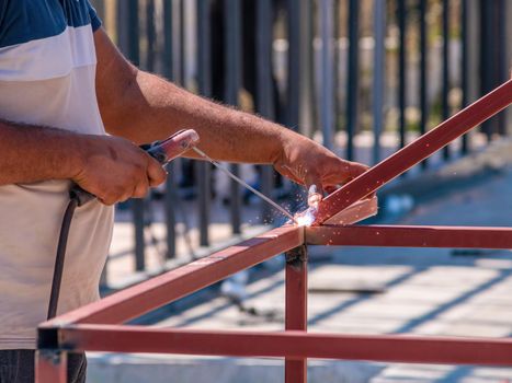 Welder welding two iron profiles at the construction site on a sunny day