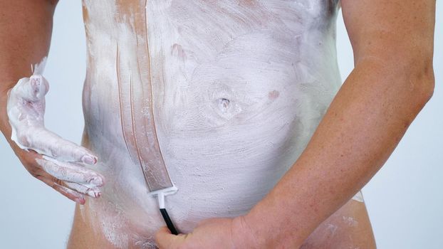 close up, caucasian Naked man shaves his body, Torso, bikini area, part of body with a razor, shaving foam. High quality photo