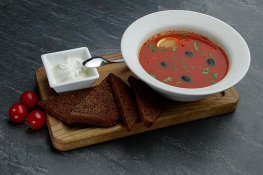 Wooden trey with meat hodgepodge, sour cream and bread on a grey background with tomatoes. High quality photo