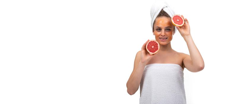 widescreen photo of a middle-aged woman after bathing procedures on a white background with an orange grapefruit in her hands.