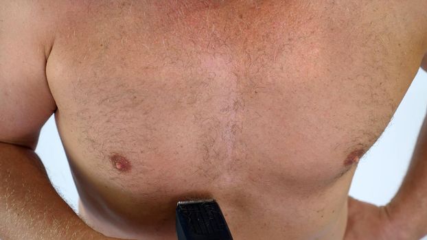 Close-up of a very hairy Man haircut body hair on his, male chest by himself with a clipper, electric razor, trimer. isolated on white background. Naked man shaves his chest. High quality photo