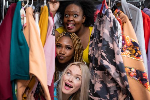 Three girls with different temperaments. Frantic clothes shopping in a shopping mall. A European woman laughs. The African shows her tongue and the other arranges her lips for a kiss.