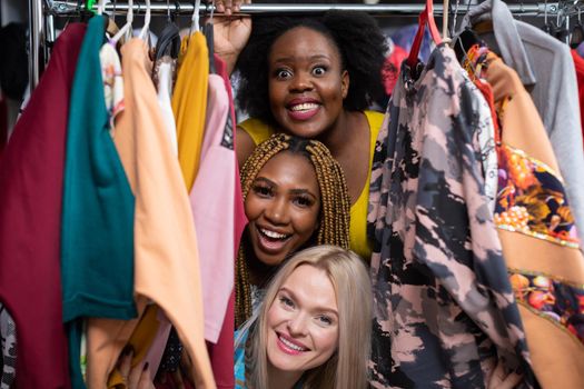 Three cheerful girls during exciting clothes shopping. Two dark-skinned women and one of Caucasian beauty. Lined up one above the other.