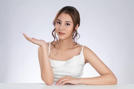 Photo of a gorgeous woman with flawless healthy fresh skin in a concept of empty space for beauty care product. Skincare product, model uses hand to create empty space for commercial.