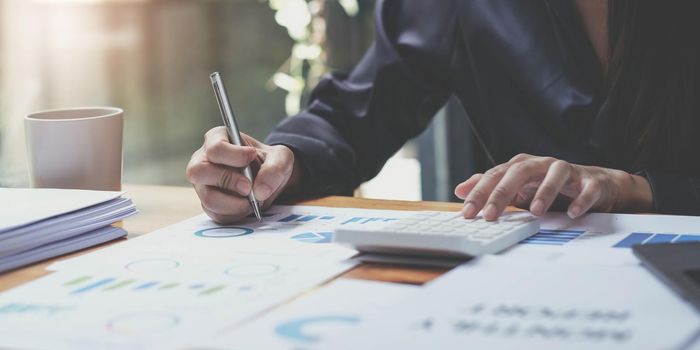 Cropped image of woman hand using calculator, working with graph chart and analyzing business strategy, financial statistic, sitting at desk office, vertical view..