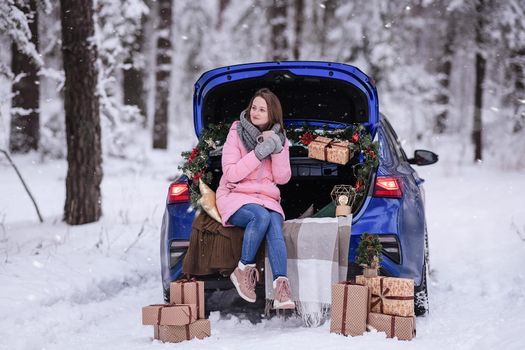 A woman in winter clothes drinks a hot drink sitting in a car decorated in a New Year's way. Traveling by car through the forest. A trip before Christmas.