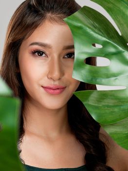 Closeup portrait of young ardent woman with healthy fair skin holding big green leaf near her face. Skin care beauty care concept.