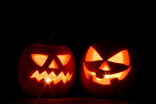 Two Halloween pumpkins with burning candles inside on black background