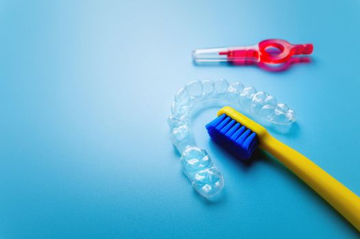 transparent plastic aligners with a yellow toothbrush and interdental brush lie on a blue background, close-up.